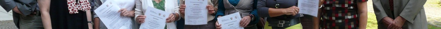 Eine Gruppe von Menschen mit Zertifikaten in der Hand posiert draußen vor einem Aufsteller von FILM+SCHULE NRW.