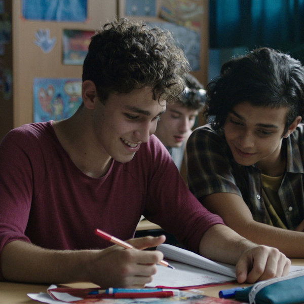 Zwei Jungen sitzen an einem Tisch in der Schule und schauen lachend auf das Heft eines Jungen.