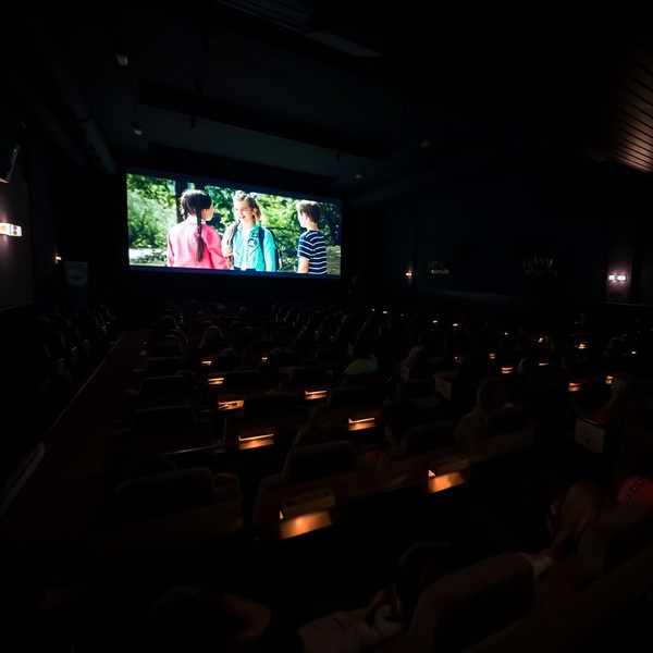 Eröffnung SchulKinoWochen NRW 2020: Ein dunkler Kinosaal, die Leinwand zeigt drei Kinder.
