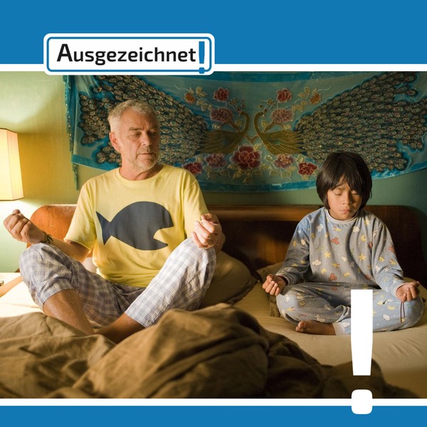 Ein kleiner Junge und ein älterer Mann sitzen im Schneidersitz nebeneinander.