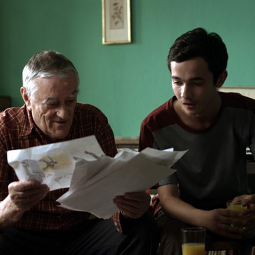 Ein junger Araber und ein älterer russischer Mann sitzen nebeneinander und schauen sich gemeinsam einen Stapel Papiere an.
