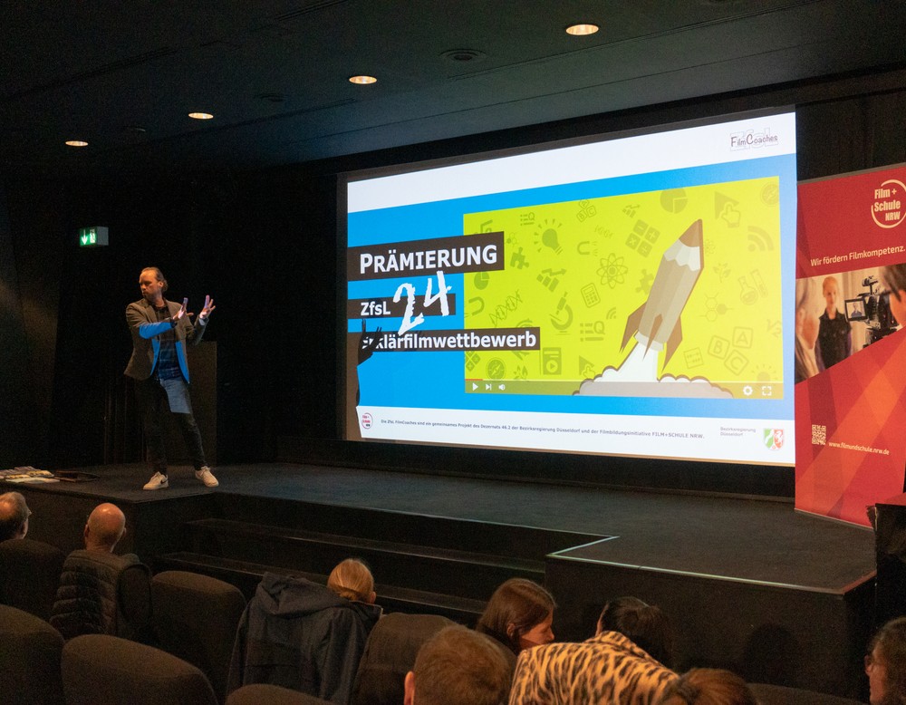 Ein Mann spricht auf der Bühne vor einer Leinwand.