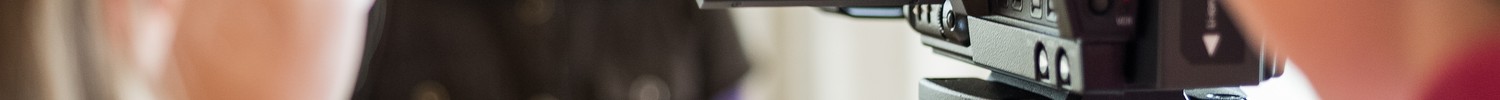 A girl is being filmed by a camera. Her face is blurry in the background, but we can see it clearly in the screen of the camera.