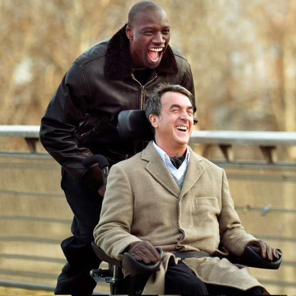 Das Filmposter des Films Ziemlich Beste Freunde. Ein schwarzer Mann schiebt einen älteren weißen Mann in einem Rollstuhl und beide lachen.