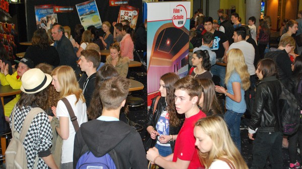 Schüler*innen stehen in einer Aula mit einem Aufsteller von Film+Schule NRW.