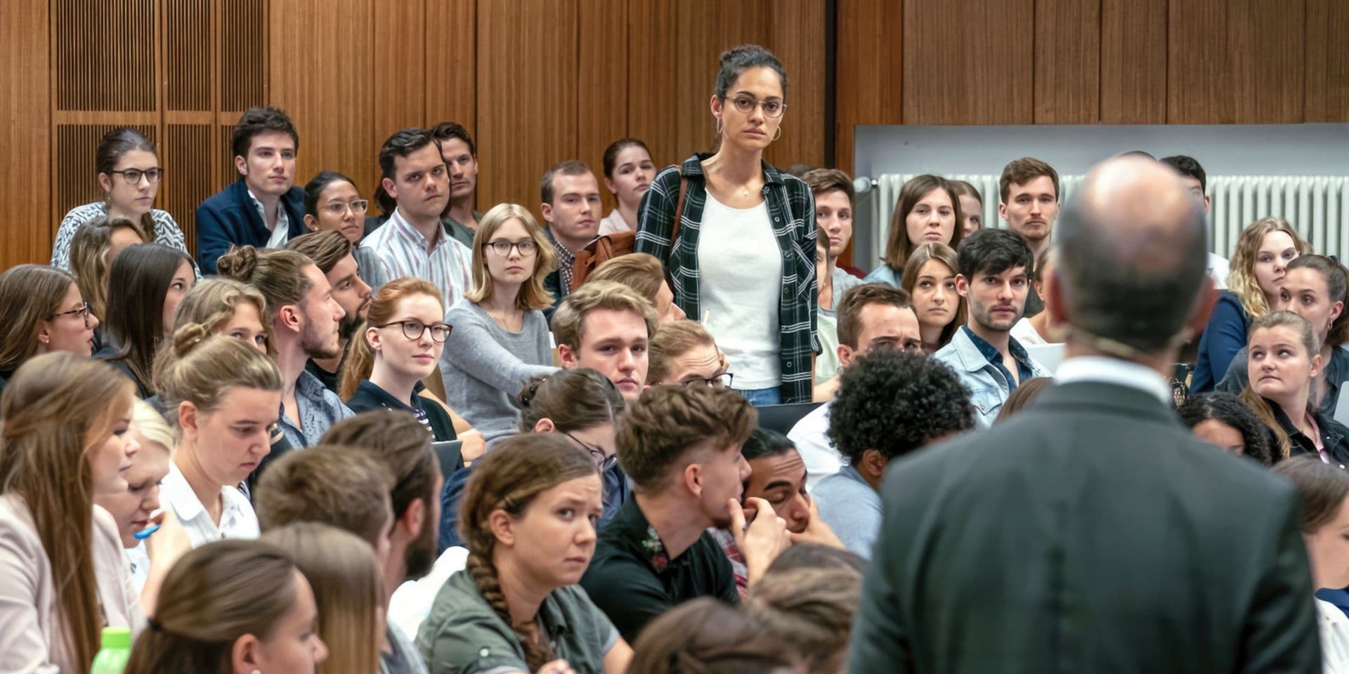 Eine Studentin und ein Professor stehen sich in einem voll besetzten Hörsaal gegenüber.