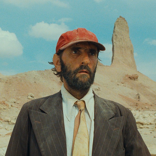 Ein Mann mit Anzug und Cappy steht in der Wüste.