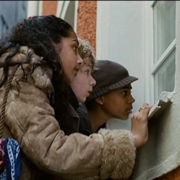 Drei Kinder schauen von außen in ein Fenster.