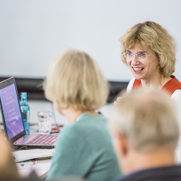 Zwei Frauen unterhalten sich in einem Seminarraum, auf dem Tisch vor ihnen steht ein Laptop.