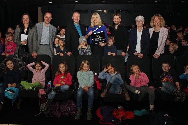 Eine Gruppe Menschen steht inmitten von Kindern in einem Kinosaal.