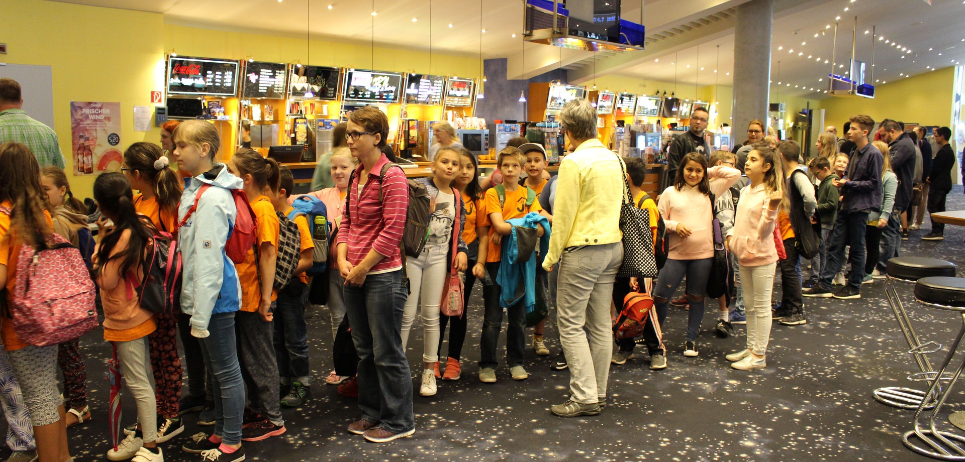 Eine Schlange aus Schüler*innen und Lehrkräften in einem Kino.