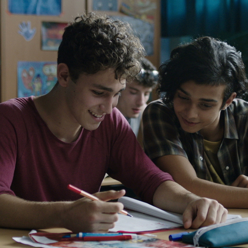 Zwei Jungen sitzen in einem Klassenraum nebeneinander, schauen auf das Heft des linken Jungen und lachen.