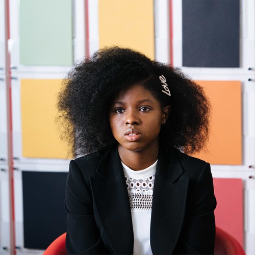 Eine schwarzes Mädchen mit einem Afro sitzt auf einem Stuhl.