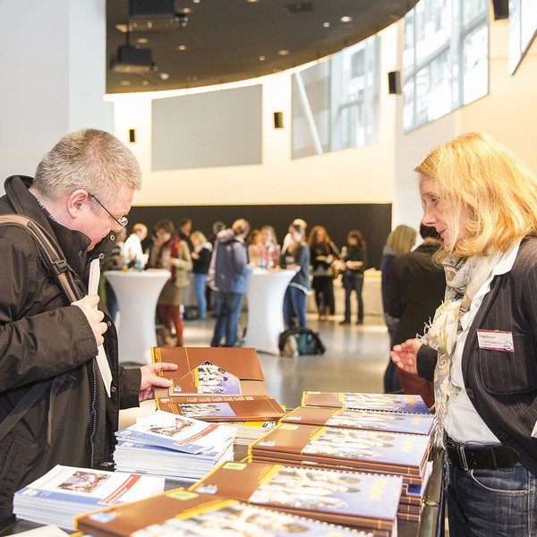 Eine Frau steht an einem Tisch auf dem Flyer ausgebreitet sind.