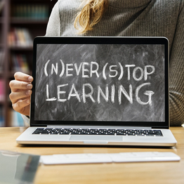 Eine Frau zeigt einen Laptop Bildschirm auf dem steht: "(N)ever (S)top Learning"