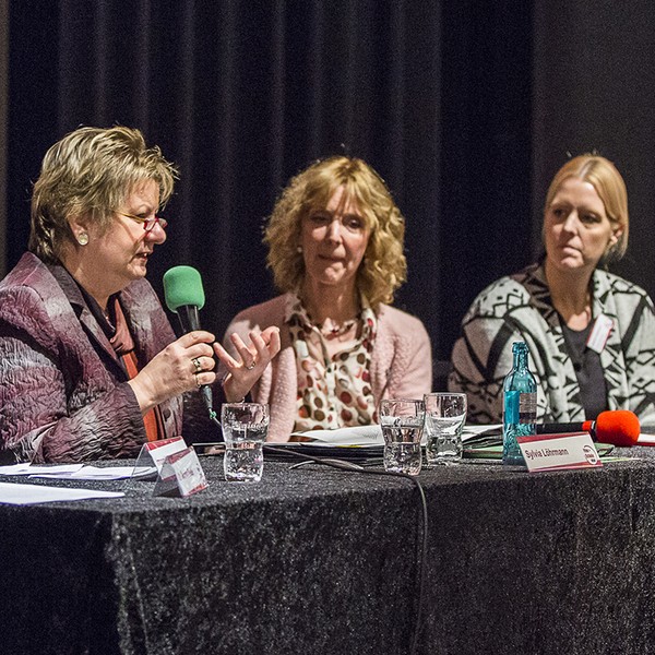 Drei Frauen sitzen an einem Podiumstisch, eine redet mit Mikrofon.