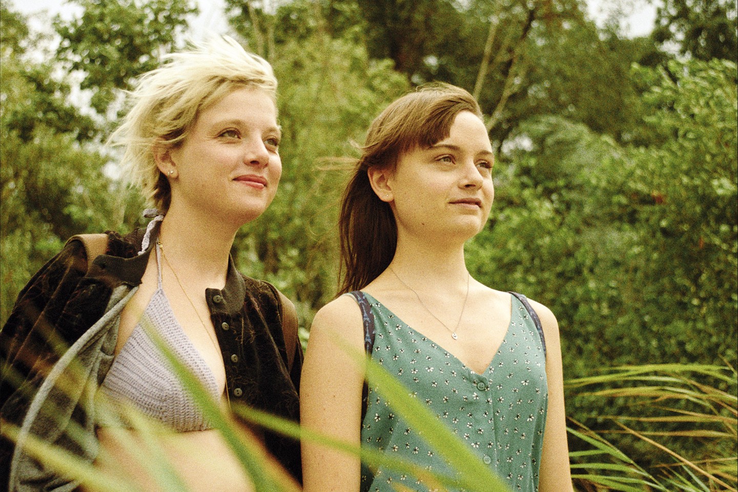 Zwei junge Frauen stehen draußen im Grünen und lächeln.