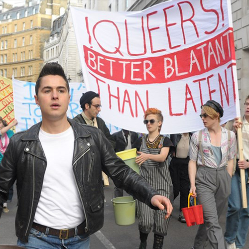 Mehrere Männer in einer Demonstration vor einem Banner mit der Aufschrift: "Queers! Better blatant than latent"