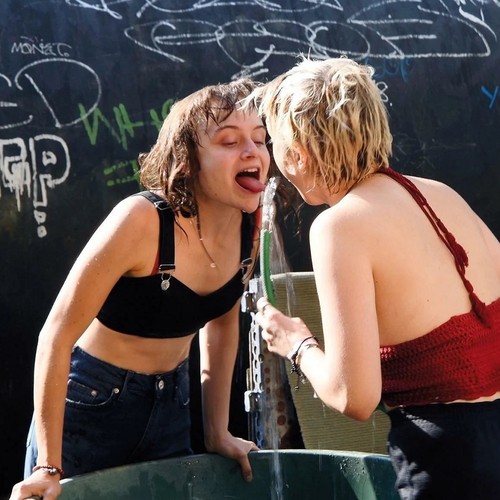 Zwei Mädchen trinken Wasser aus einem Gartenschlauch.