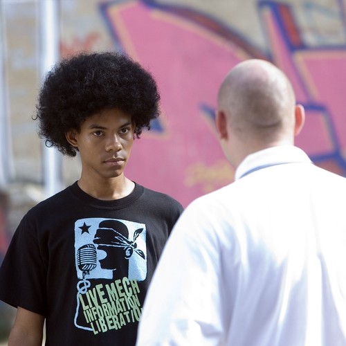 Ein Junge mit einem Afro steht einem Mann mit Glatze gegenüber.