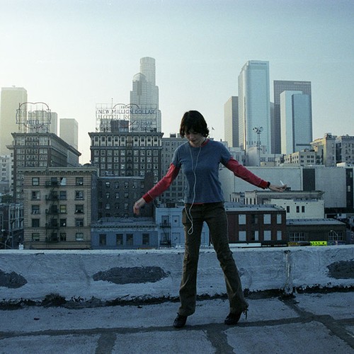 Eine junge Frau tanzt auf einem Hausdach vor der Skyline einer Stadt.