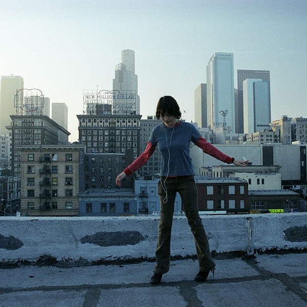 Eine junge Frau tanzt auf einem Dach vor einer städtischen Skyline.