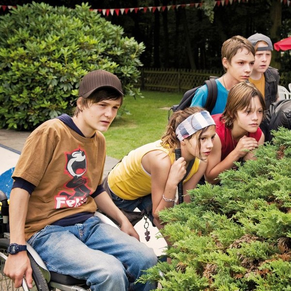 Eine Gruppe Kinder hockt hiner einem Busch und späht darüber.