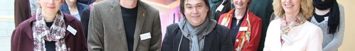 Eine Gruppe Menschen posiert um einen Aufsteller von FILM+SCULE NRW.